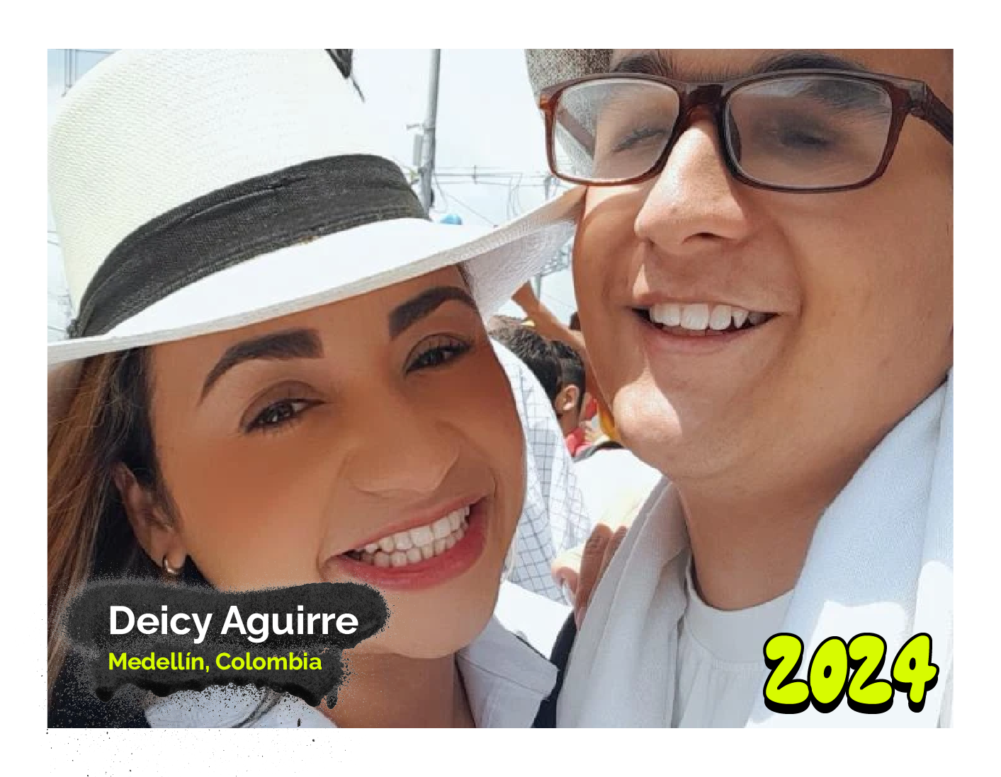 Fotografía de Deicy Aguirre, de Medellín, Colombia, sonríe ampliamente junto a una persona en una selfie al aire libre, en un día soleado. Ella lleva un sombrero blanco con una banda negra y maquillaje natural, mientras él lleva gafas y una camisa clara. Texto en la imagen: año '2024'.