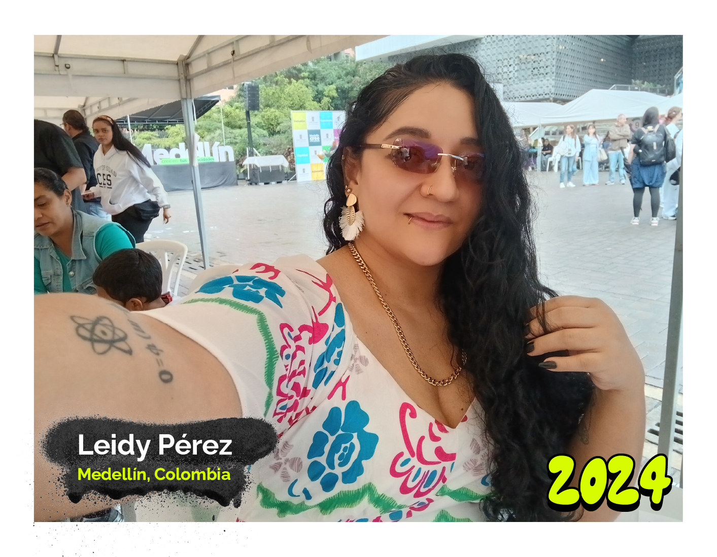 Fotografía de Leidy Pérez, mujer de cabello rizado y largo, con gafas de sol y blusa estampada colorida, posa sonriendo en un evento al aire libre. Abajo, el texto dice: Medellín, Colombia' y año '2024´.