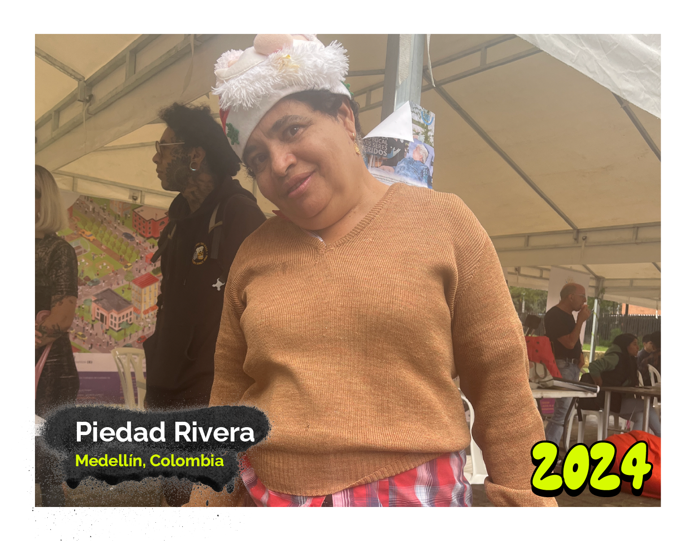 Fotografía de Piedad Rivera, mujer sonriente vestida con un suéter beige y una falda de colores, posando bajo una carpa. Lleva un gorro de Navidad decorado con detalles blancos. En la esquina inferior izquierda, un texto dice 'Medellín, Colombia', y en la esquina inferior derecha aparece el año '2024'."